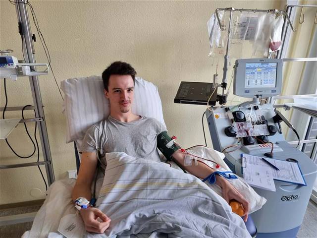 Lukas in a hospital chair during a stem cell donation, connected to an apheresis machine, smiling