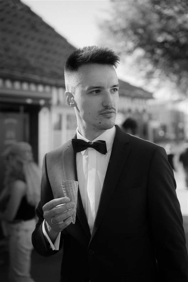 Black-and-white portrait of Lukas in a tuxedo, holding an ice cream cone and looking off to the side