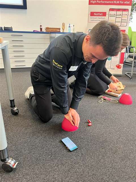 Lukas kneeling on the floor at a CPR training, pressing on a red training pad