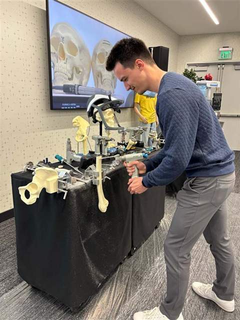 Lukas at a demo table, holding a surgical power tool over an anatomical training model